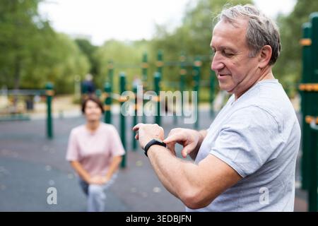 Elderly man looking at his smart bracelet in open-air sports area Stock Photo