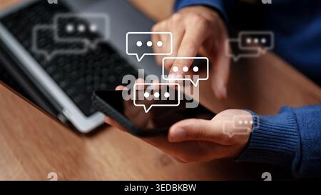 Sending messages on a smartphone while sitting at a desk with a computer nearby Stock Photo