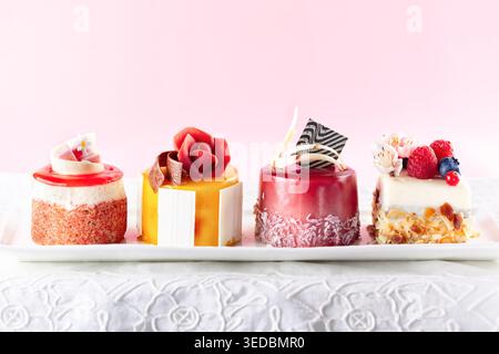 Various mini cakes on a white plate. Sweets decorated with fresh berries and flowers for holiday. Stock Photo