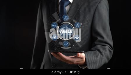 A businessman in a suit showcases innovative agile methodology icons in a digital presentation. The dark background emphasizes the modern approach to Stock Photo
