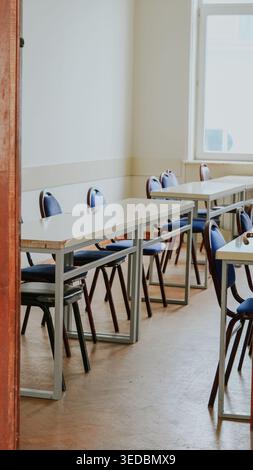 An empty classroom with rows of desks and blue chairs in a bright, academic setting Stock Photo