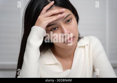 Headache, female having migraine pain, bad health, Asian woman feeling stress and headache, Office syndrome, sad tired touching forehead having migrai Stock Photo