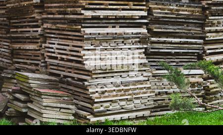 Large stack of weathered wooden planks and boards outdoors on green grass. Stock Photo