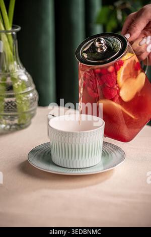 Pouring fruit tea from glass teapot into cup Stock Photo