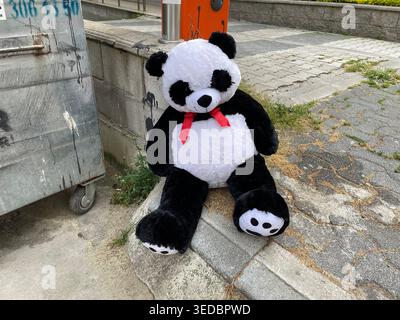 Black and white plush panda toy placed on a city sidewalk curb near street, abandonment, childhood. Stock Photo