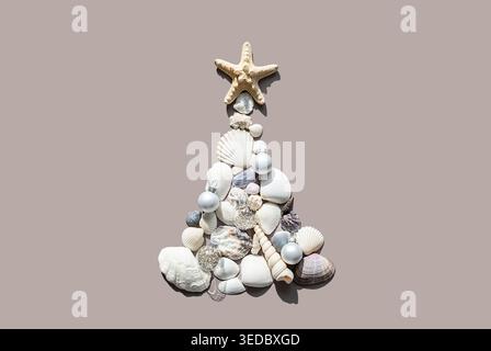 Christmas tree made of sea shells and starfish on beige background. Creative holiday decoration for winter vacation concept. Tropical celebration of N Stock Photo