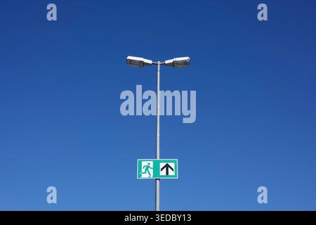 emergency exit to heaven with direction sign on street lamp post against blue sky Stock Photo