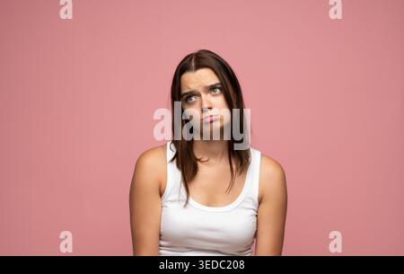 Frustrated young woman looking up, feeling bored and thinking, expressing sadness or disappointment with a pout Stock Photo