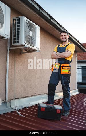 Confident HVAC technician standing on a rooftop after successfully installing an air conditioning unit Stock Photo