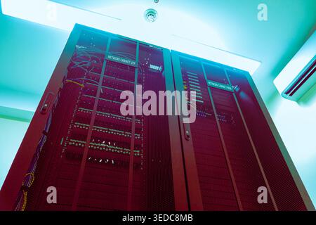 View of a tall server rack in a data center, showcasing networking equipment and cables under soft ambient lighting, emphasizing modern technology and Stock Photo