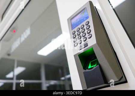 A close-up image of a modern fingerprint scanner mounted on a white wall. The device features a keypad and green light, symbolizing advanced security Stock Photo