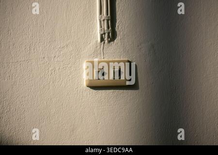 A minimalist wall features two electrical switches casting subtle shadows on the textured surface, highlighting the interplay of light and design in a Stock Photo