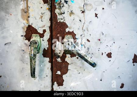 Close-up view of rusty metal door handles on an old, weathered surface. Displaying peeling paint and layers of texture, this image captures vintage ch Stock Photo