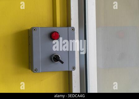 A close-up of an electrical control panel featuring a prominent red button and a toggle switch mounted on a vibrant yellow wall. Ideal for tech and de Stock Photo