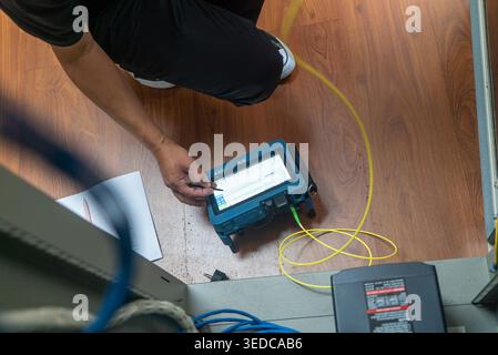 A technician carefully tests network equipment using a cable tester, showcasing hands-on analysis in a modern workspace with digital tools. Stock Photo