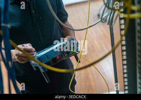 A technician carefully tests network equipment among tangled cables and wires in a modern workspace, ensuring proper functionality and connectivity. Stock Photo
