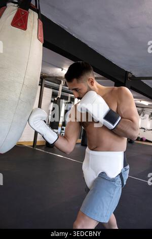 Male boxer training hard, practicing punches with gloves on a heavy bag Stock Photo