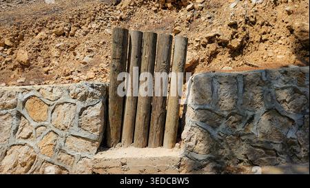 Vertical wooden logs built into a stone retaining wall illustrating rural construction texture materials craftsmanship and sustainable outdoor design Stock Photo