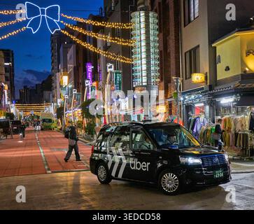 Uber taxi cab drives in Asakusa district brightly illuminated at night. Taito City, Tokyo, Japan. Stock Photo