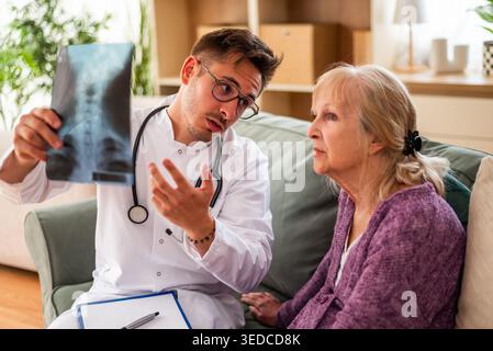Home doctor is examining x-ray image with elderly woman at her home. Professional health support for elderly people. Stock Photo