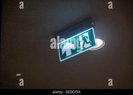 Bright green emergency exit sign with an upward arrow and a running figure, designed to guide individuals safely during emergencies in indoor spaces. Stock Photo