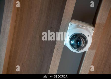 A close-up view of a ceiling-mounted security camera showcasing modern design and technology in indoor surveillance systems for safety and monitoring. Stock Photo