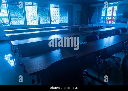 This image captures an empty classroom setting with desks and chairs arranged in a neat layout, illuminated by soft, blue light filtering through the Stock Photo
