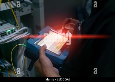 A technician uses a portable network testing device, featuring a touchscreen interface, in a data center environment to monitor and analyze connection Stock Photo