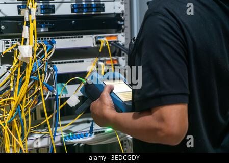 A network technician uses testing equipment to check wiring connections inside a data center, ensuring optimal performance and connectivity in modern Stock Photo