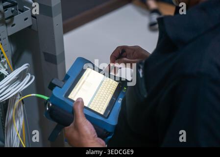 A technician uses a portable touchscreen device to analyze network connections and diagnose issues in a high-tech workspace, ensuring optimal performa Stock Photo