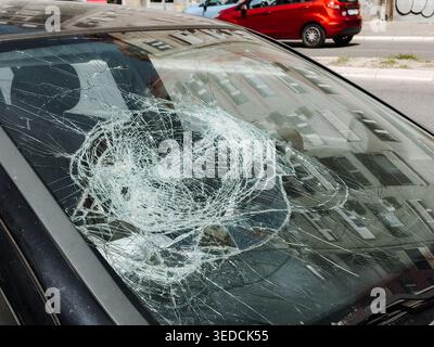 Broken windshield with heavy impact cracks parked on city street. Urban accident damage concept for insurance, transport risk, safety and vehicle Stock Photo