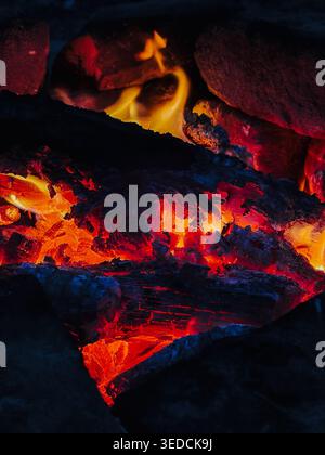 Glowing firewood burns with bright orange flames in close detail. Warm heat concept for fireplace, winter comfort, energy and natural fire texture. Stock Photo