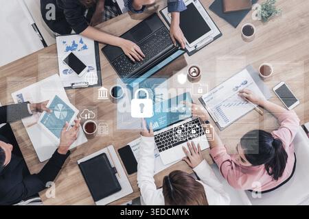 A diverse group of professionals engages in a collaborative business meeting focused on data security innovation, utilizing laptops and digital Stock Photo
