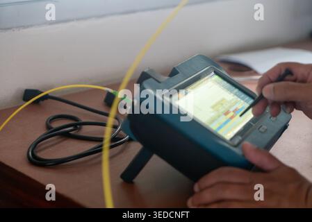 A technician using a portable device to measure and analyze data on a screen with cables connected. This tool showcases modern technology in diagnosti Stock Photo