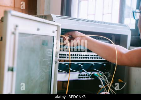 A technician performs maintenance on a network cabinet, managing connections and cables for optimal data flow and communication in an office setting. Stock Photo