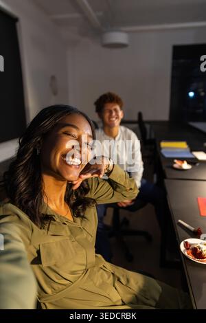 Diverse coworkers taking selfie beside table in conference room with smartphone and notebooks Stock Photo