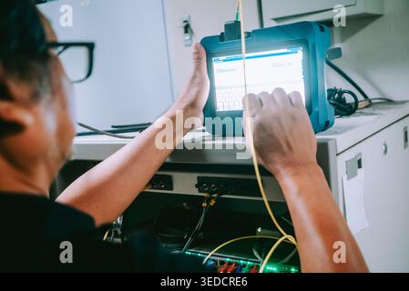 Technician focuses on a measurement tool while testing connections in a professional workspace. The device displays critical data for analysis and per Stock Photo