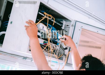 Technician organizes cables within a network cabinet, showcasing wiring management for optimal office connectivity and efficiency in a modern workspac Stock Photo