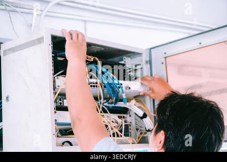 A technician works on network equipment inside a cabinet. Cables are carefully organized as the technician ensures proper connectivity and performance Stock Photo