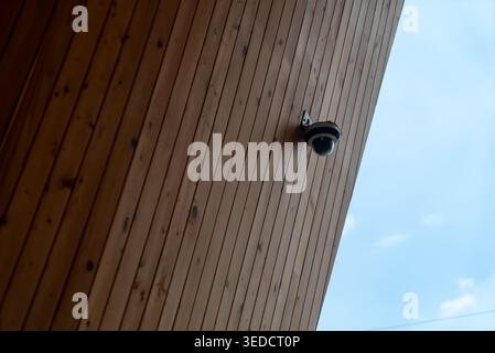 A security camera mounted on a wooden wall, showcasing modern surveillance technology. The image highlights architectural design and safety features i Stock Photo