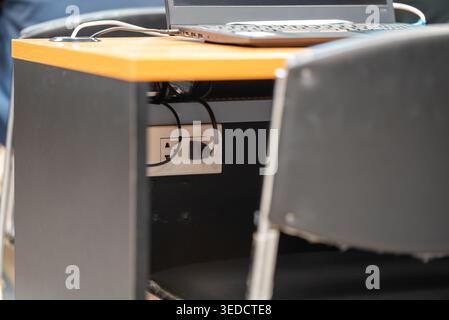 A modern workspace featuring a laptop on a stylish desk with an electric outlet. This setup emphasizes convenience and functionality for work tasks. Stock Photo