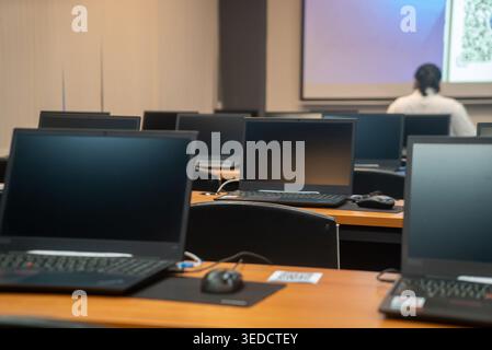 A modern classroom setup featuring rows of empty desks with laptops. The space is designed for educational sessions, workshops, or training events. Stock Photo
