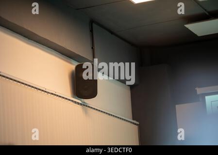 A black audio speaker is mounted on a gray wall indoors, showcasing modern technology for sound performance and acoustic quality in various environmen Stock Photo