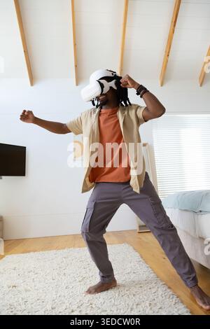 African American man standing in loft bedroom wearing white VR headset and interacting with VR Stock Photo