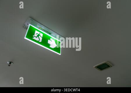 A bright green emergency exit sign with an arrow is mounted on the ceiling, providing clear direction for safe evacuation in case of emergencies. Stock Photo