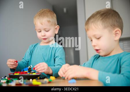 Two boys playing with building blocks, assembling colorful pieces and creating model. Sitting at table at home, creative play, learning and sibling interaction Stock Photo
