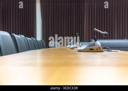 A modern conference room featuring a long wooden table, microphones, and empty chairs, set up for a professional meeting or discussion. Stock Photo