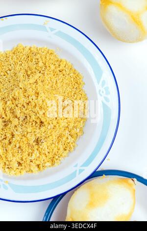 A top view of grated lemon peel served on a patterned plate, with peeled lemons placed nearby on a clean white background. Stock Photo