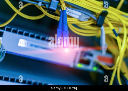 This close-up image captures vibrant fiber optic cable connections in a data center, showcasing modern technology and efficient data transmission path Stock Photo