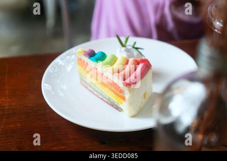 A vibrant slice of rainbow cake on a white plate features colorful layers and a light cream topping. Perfect for celebrations and desserts. Stock Photo